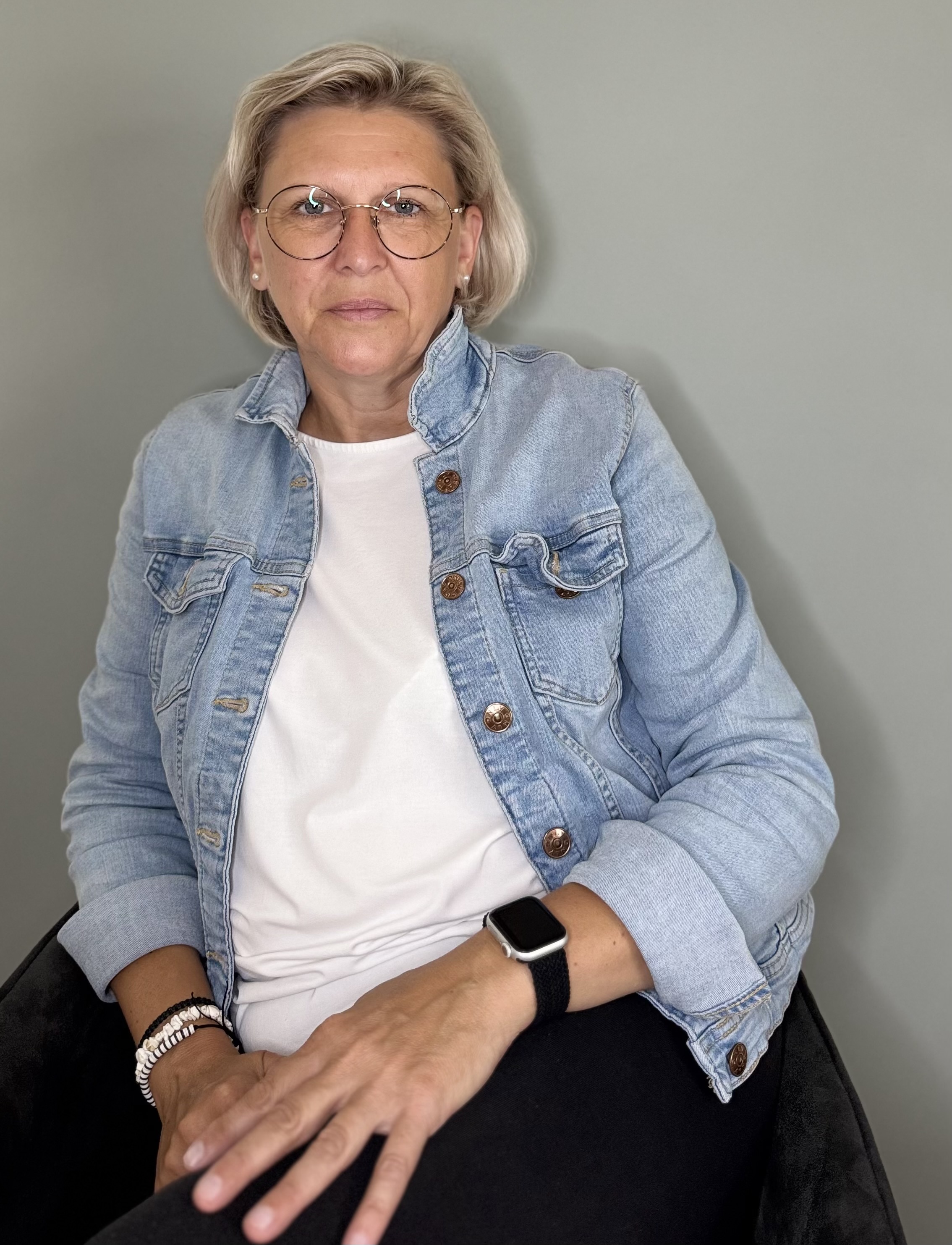 Porträt mit Brille und Jeansjacke vor grauem Hintergrund